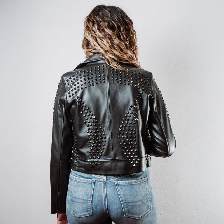 Mujer usando chamarra biker de piel negra con estoperoles negros modelo 'Rockstar Oscura' de Gerhel. Vista trasera.